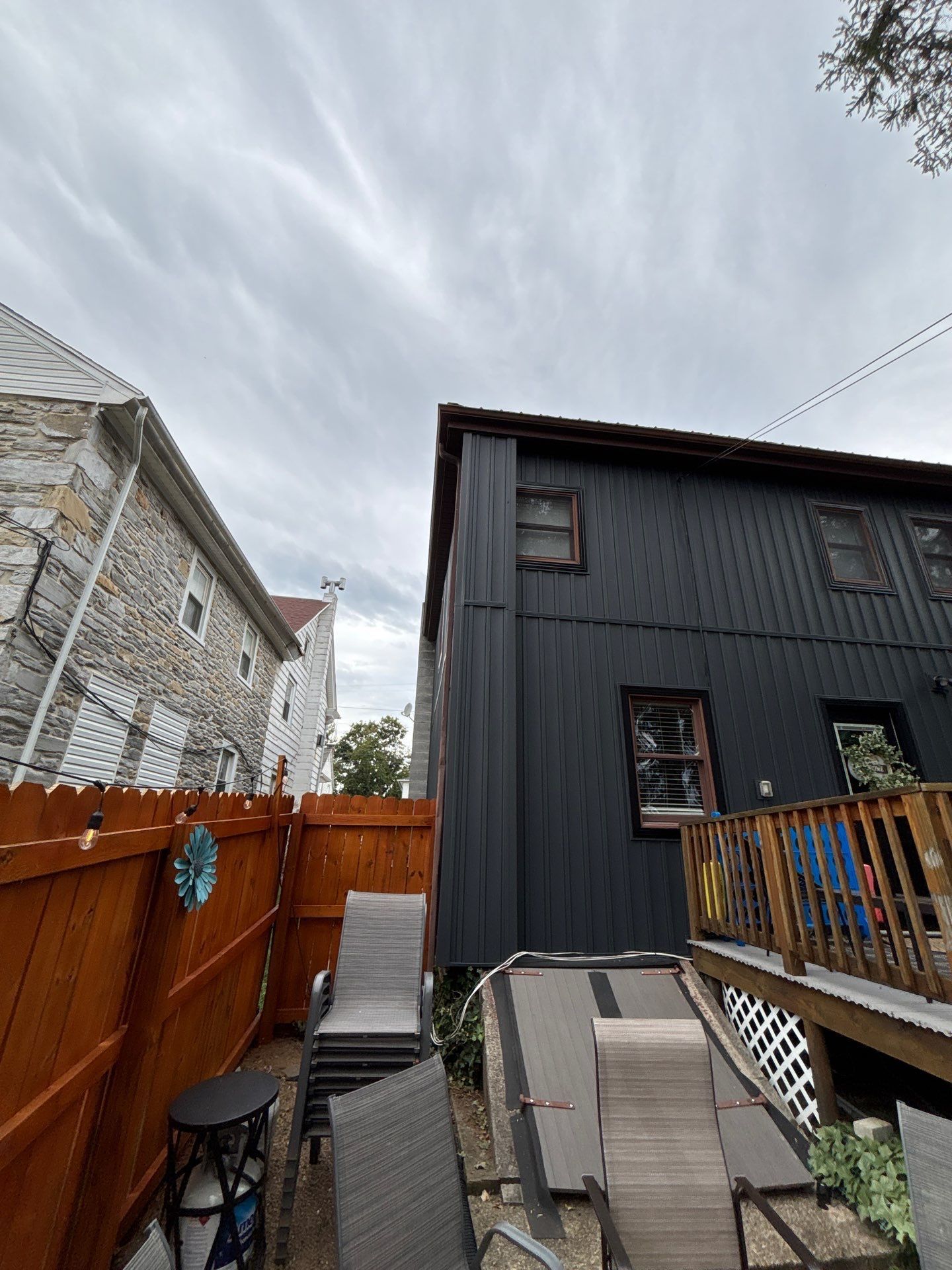 Backyard between two houses with a wooden fence, ramp, and dark gray siding under a cloudy sky