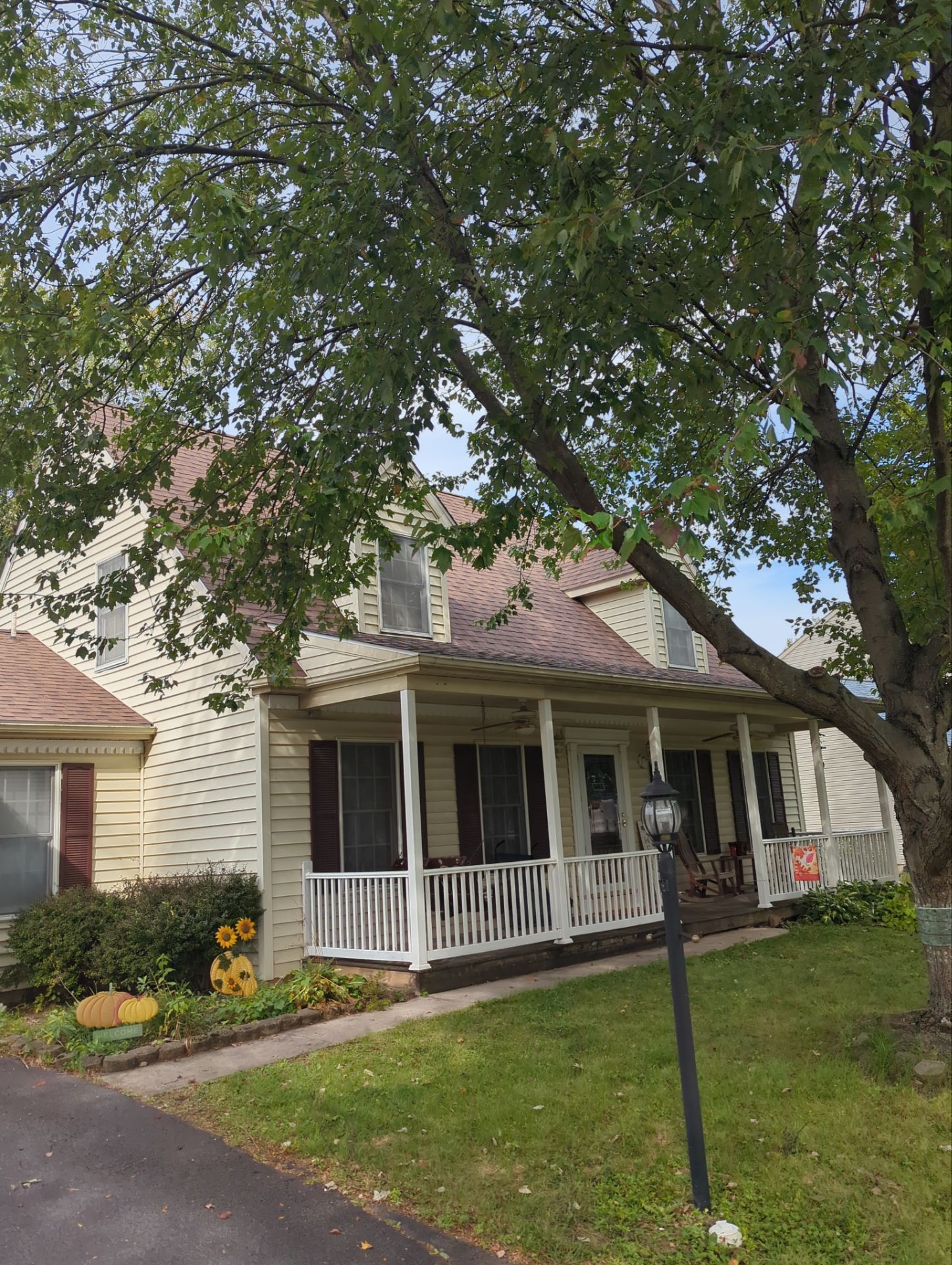 Suburban house with a front porch, white railing, and a large tree shading the yard