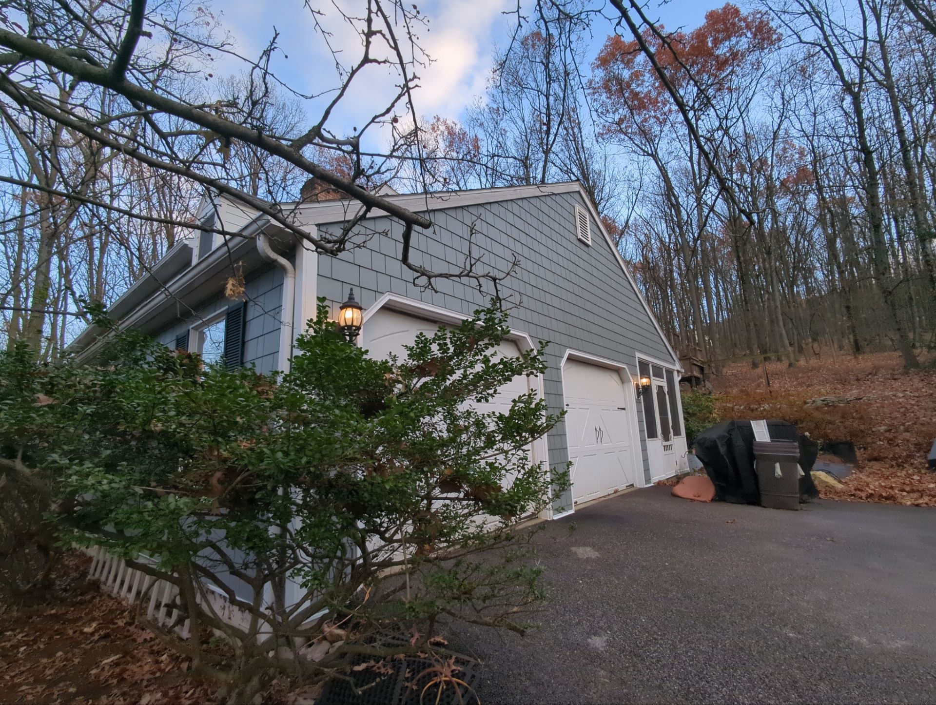 House with gray siding and roof, trees in the background, driveway in the foreground.