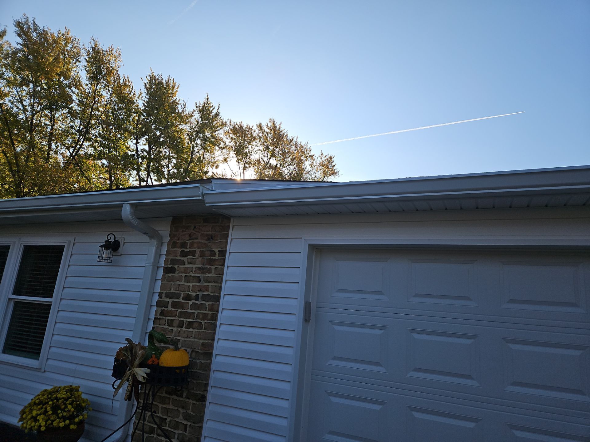 House exterior with brick and white siding, garage door, and autumn trees under a clear blue sky