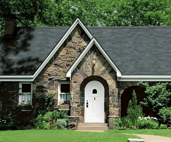 Two-story house with red siding, wrap-around porch, and turret under a gray roof with a flowering tree in front.
