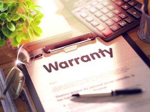 Warranty document on a clipboard, with a calculator, pen, glasses, and plant in the background.