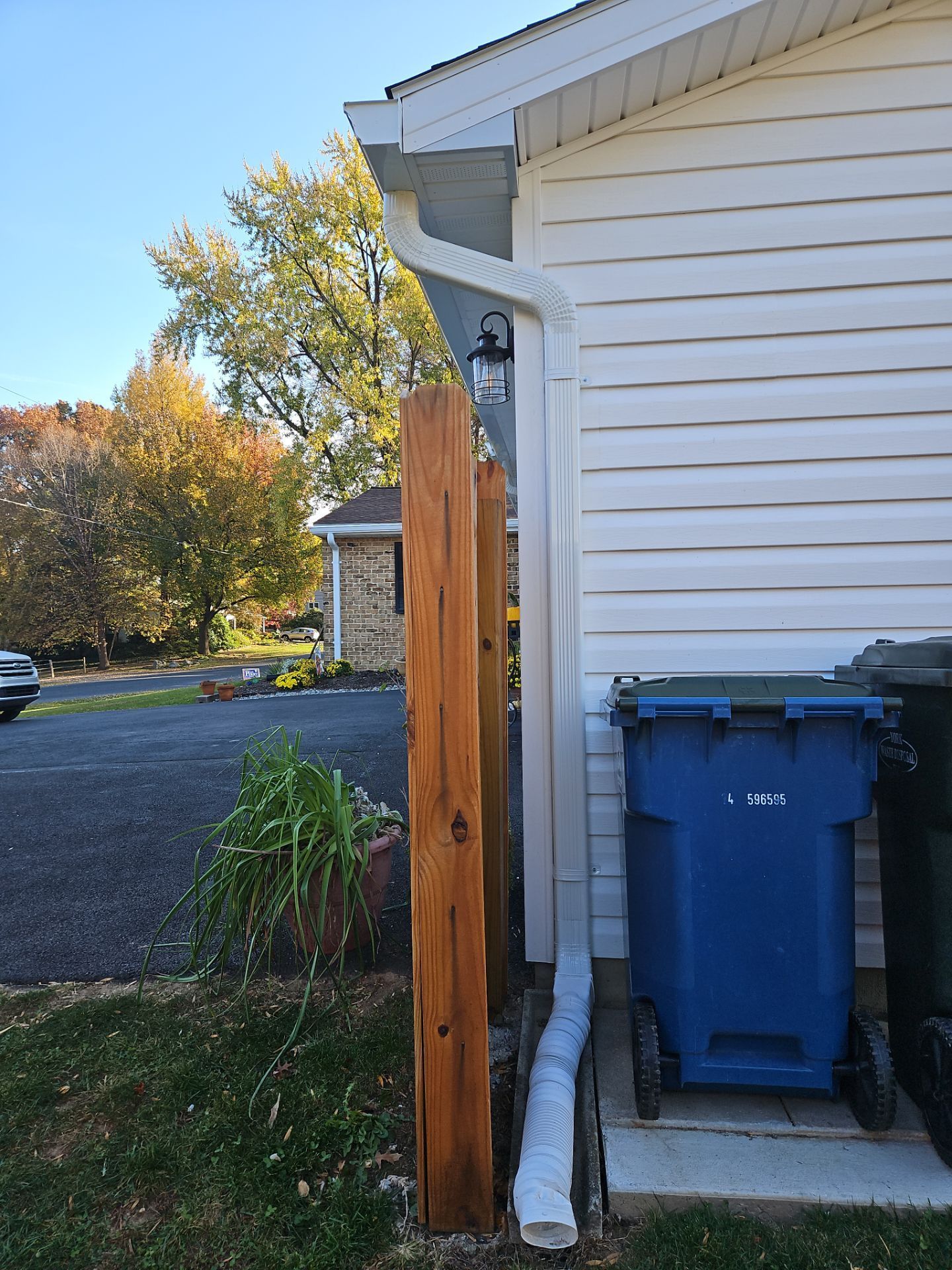 Backyard side of a house with a blue recycling bin, wooden post, and driveway