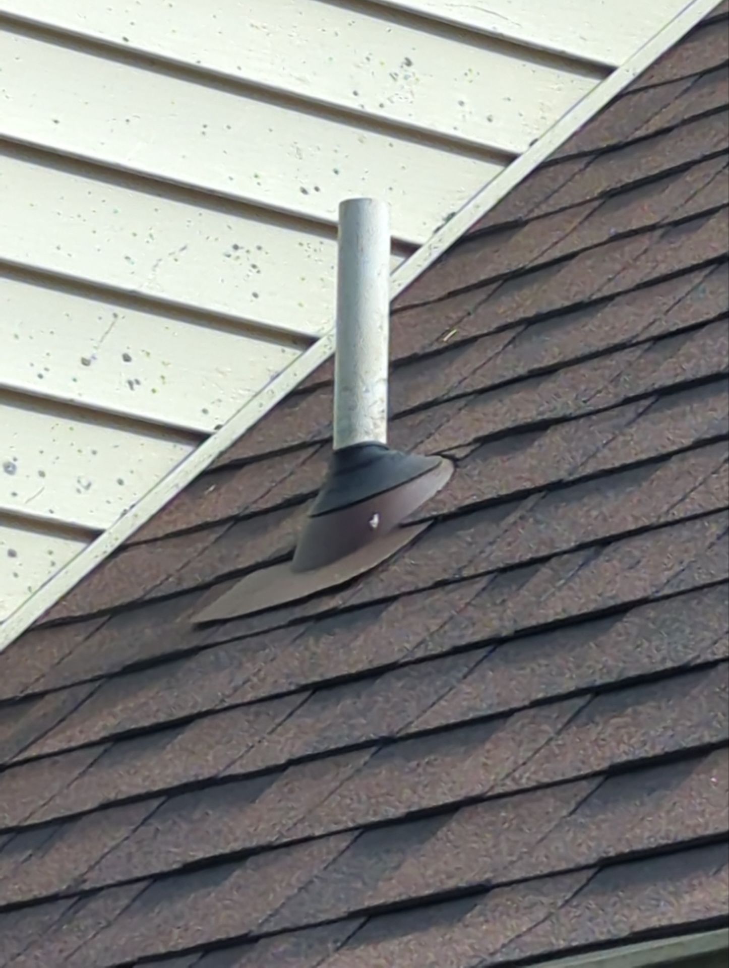 Metal chimney vent on a shingled roof beside white soffit panels