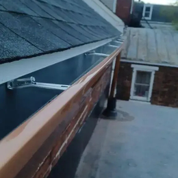 Copper gutters along a dark shingle roof edge, with a glimpse of neighboring buildings.