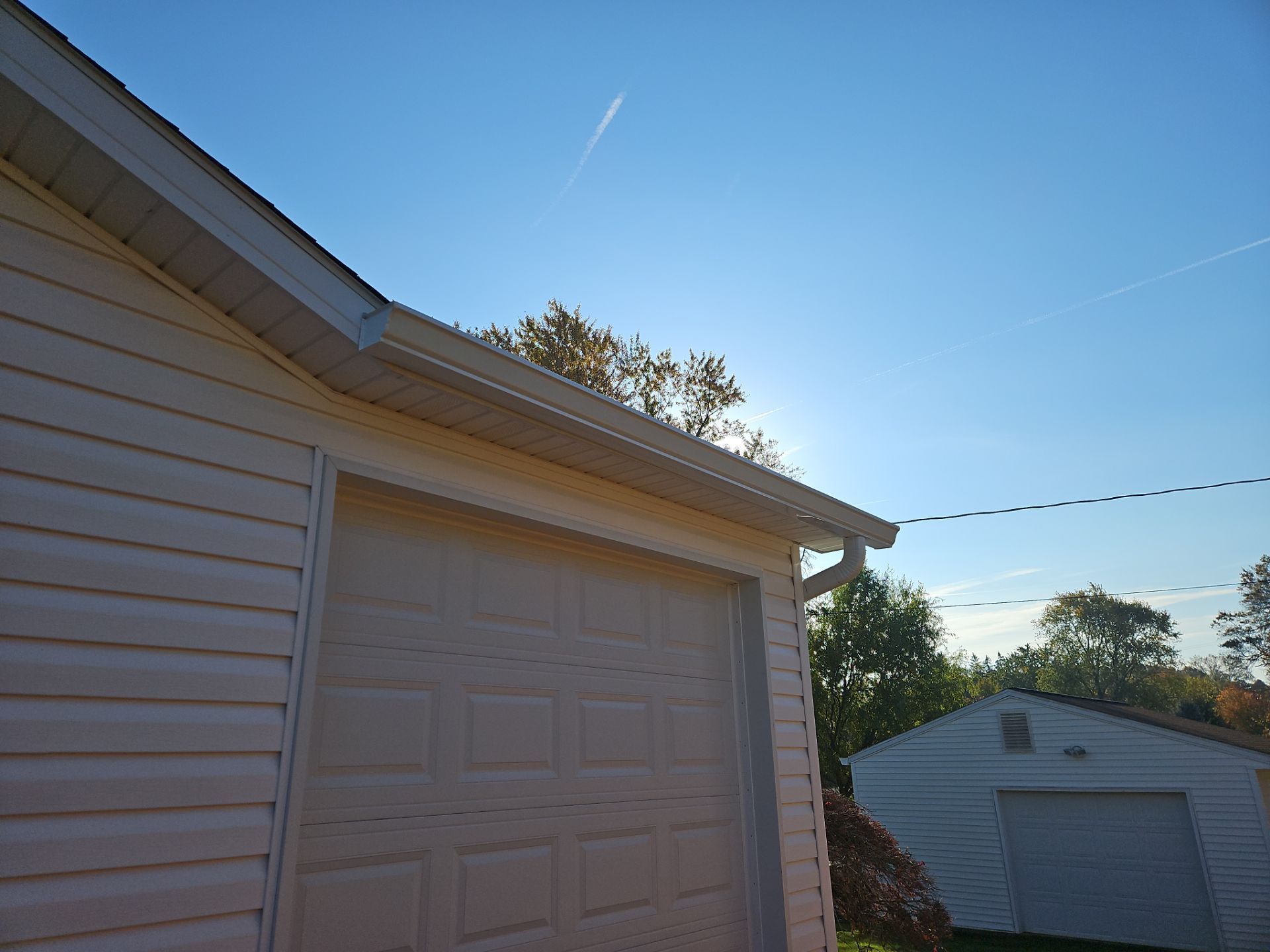 Two white garage doors on beige buildings under a blue sky at sunset