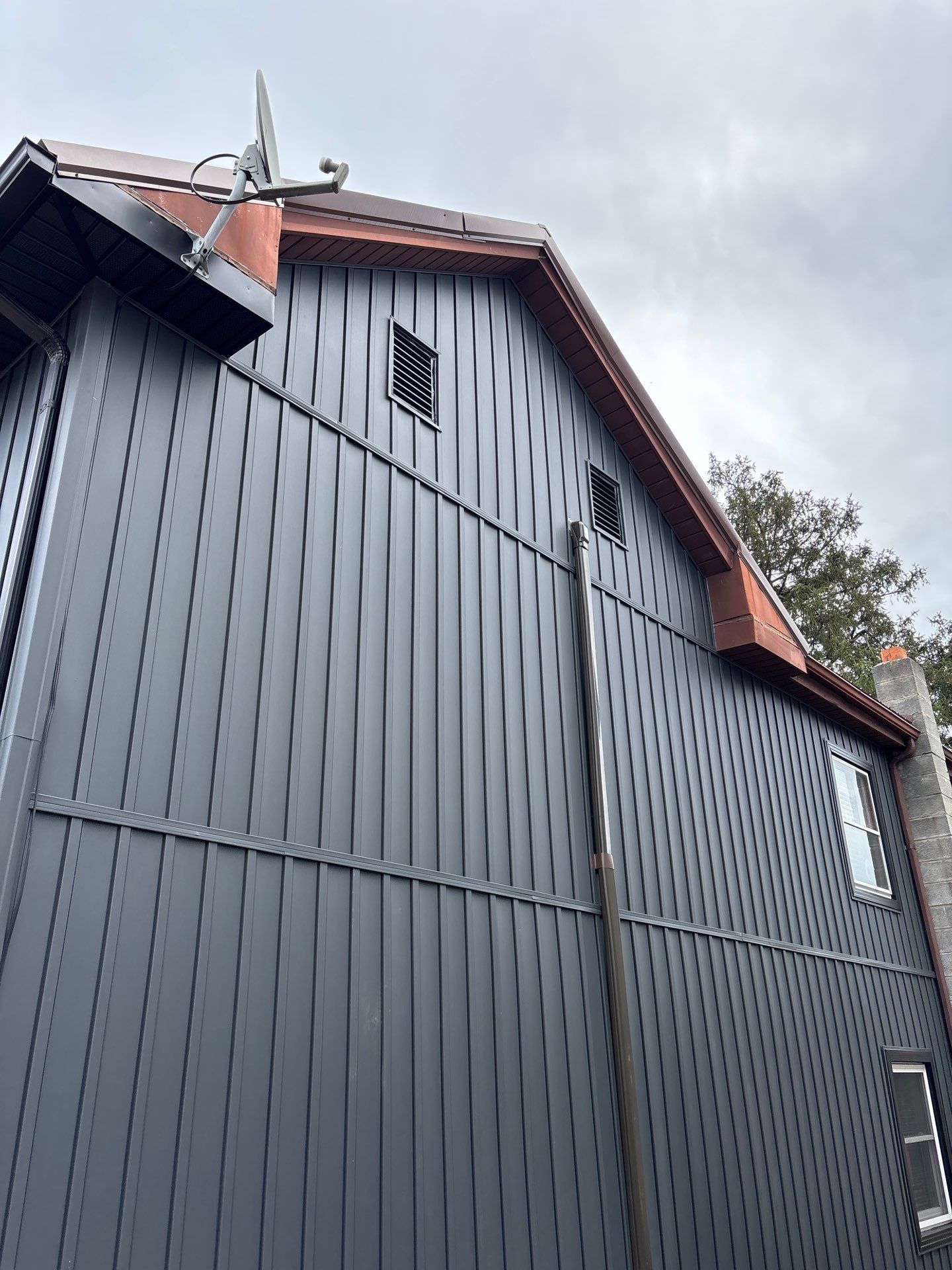 Dark gray wooden building with a red roof and overcast sky, viewed from below