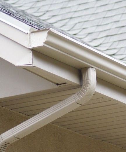 White rain gutter and downspout attached to a house roof edge