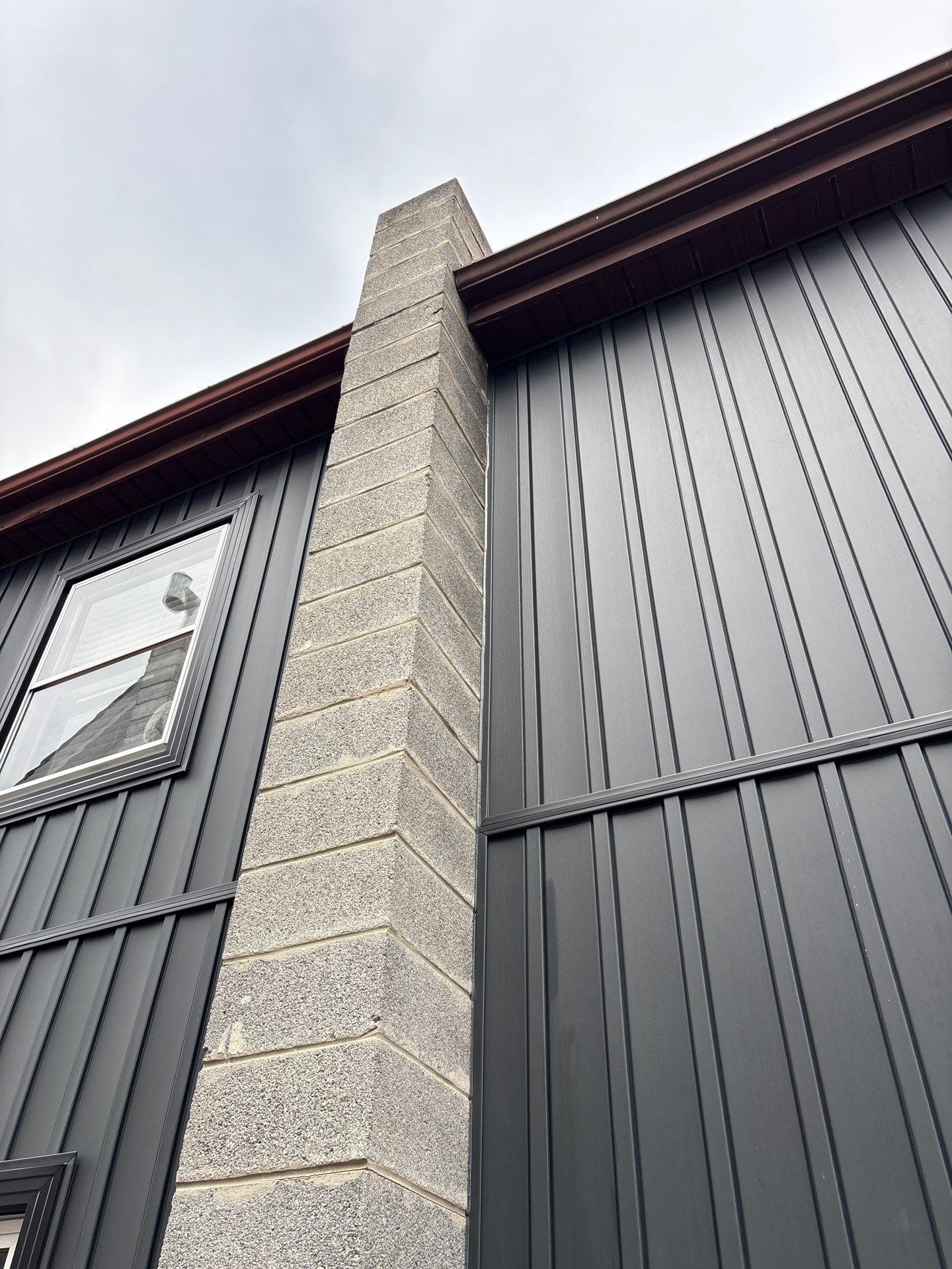 Exterior of a modern building with dark siding and a stone chimney viewed from below