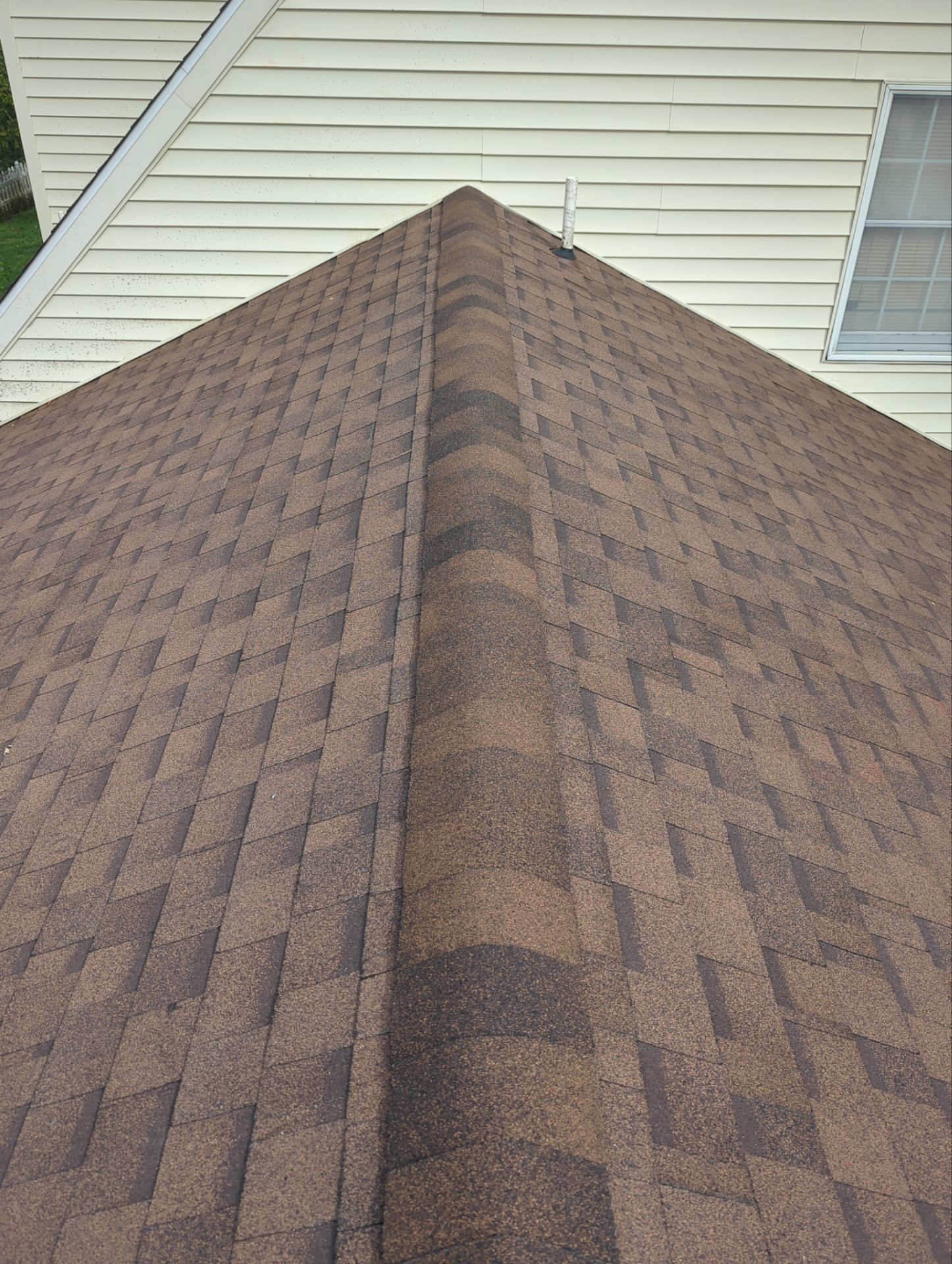 Close-up of a brown shingle roof ridge against light-colored house siding.
