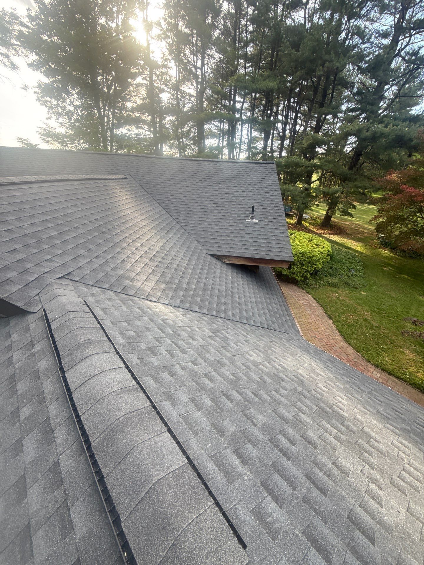 Gray shingle roof with trees and lawn beside it on a sunny day