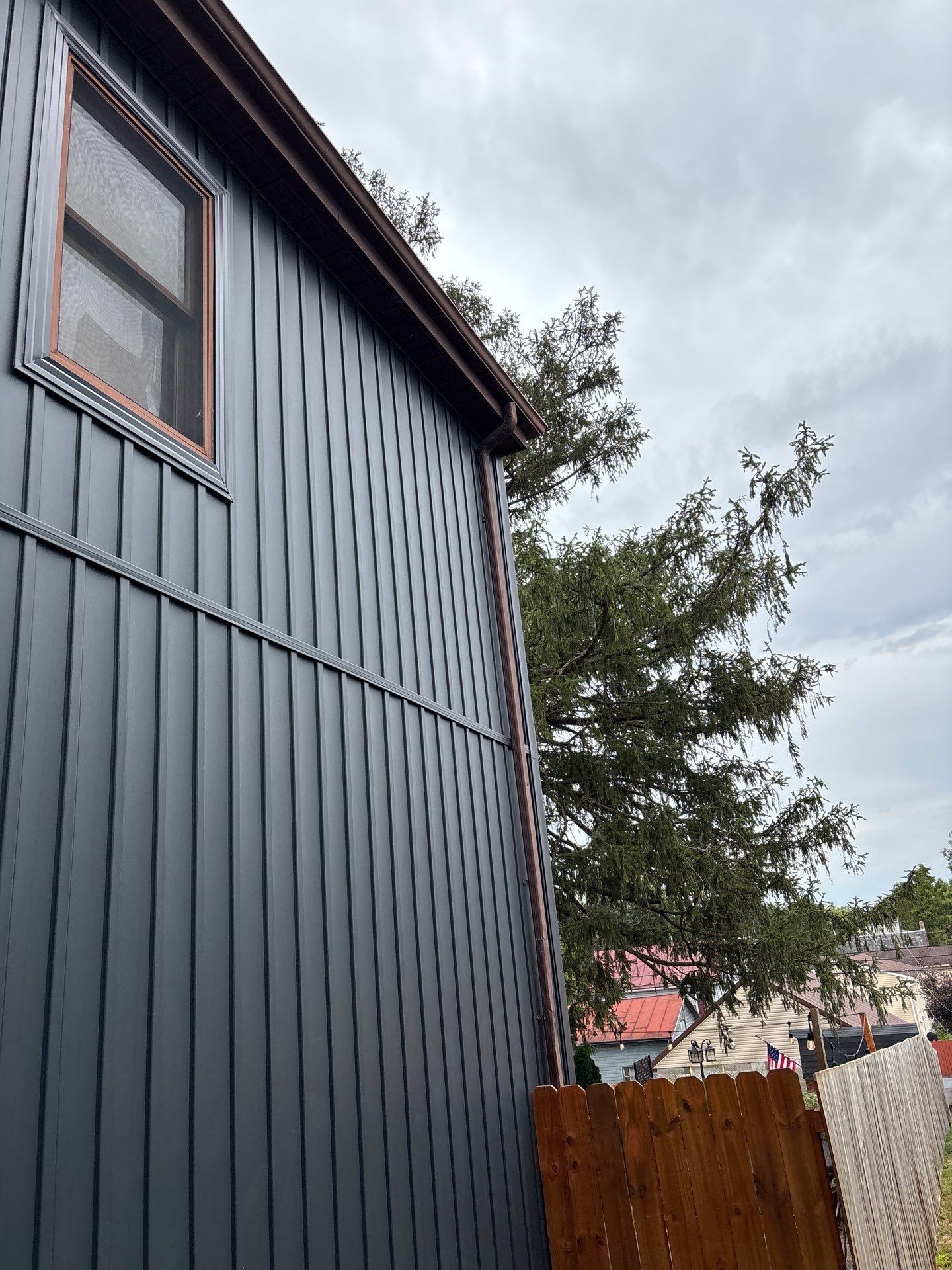 Dark blue house exterior with a window, fence, and trees under a cloudy sky