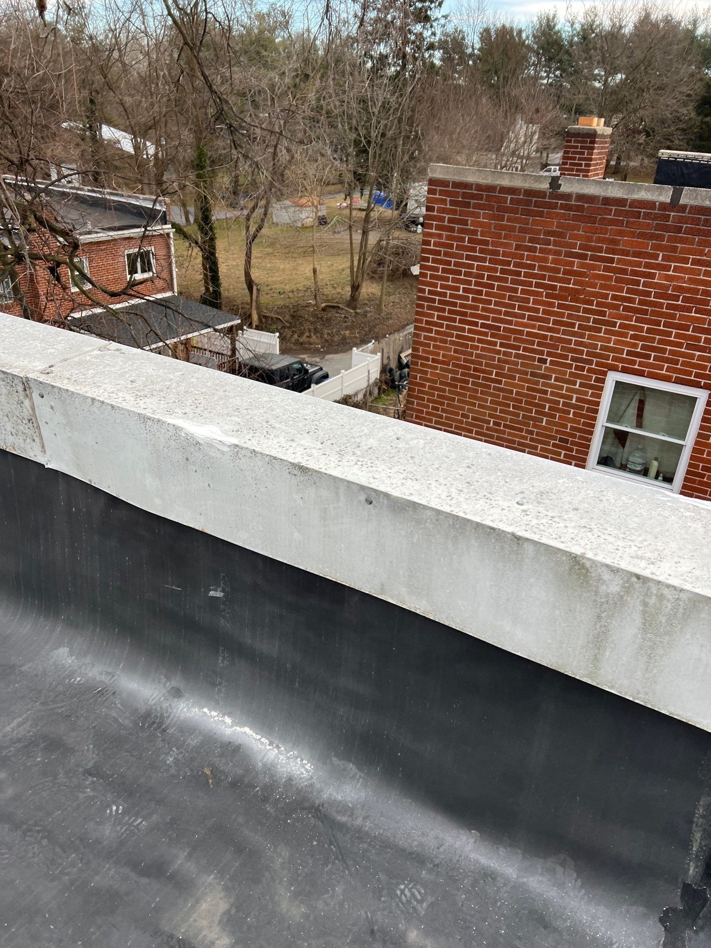 Flat black roof with concrete trim, overlooking a yard and brick building.