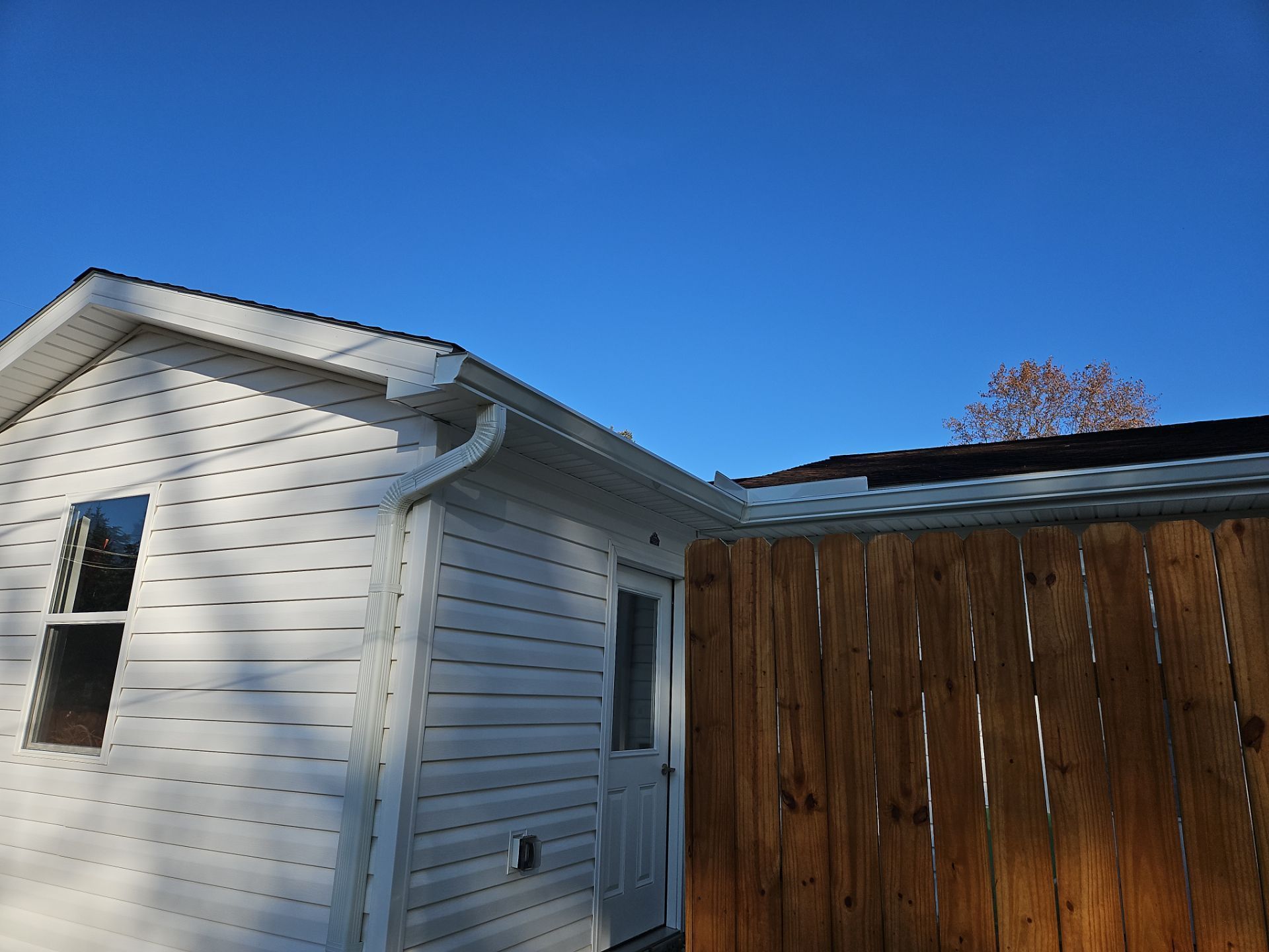 White house siding beside a wooden fence under a clear blue sky