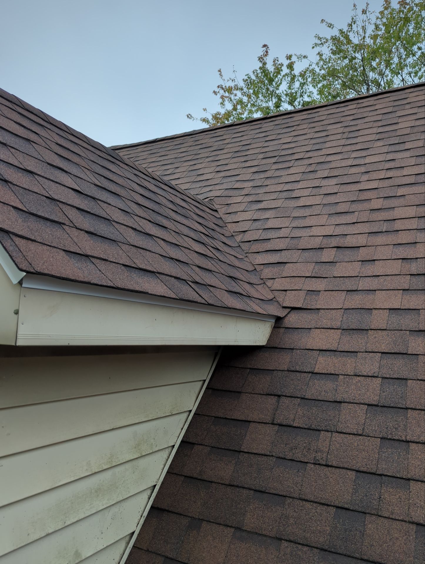 Roof shingles meeting at an exterior house corner with beige siding and blue sky above