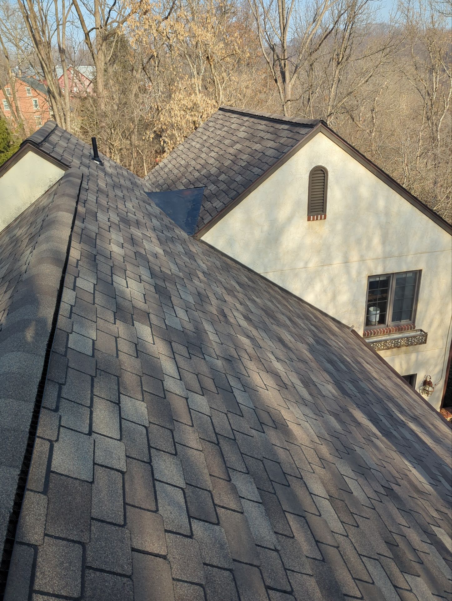 Asphalt shingle roof with varying shades of brown. Building with beige stucco and a small arched window.