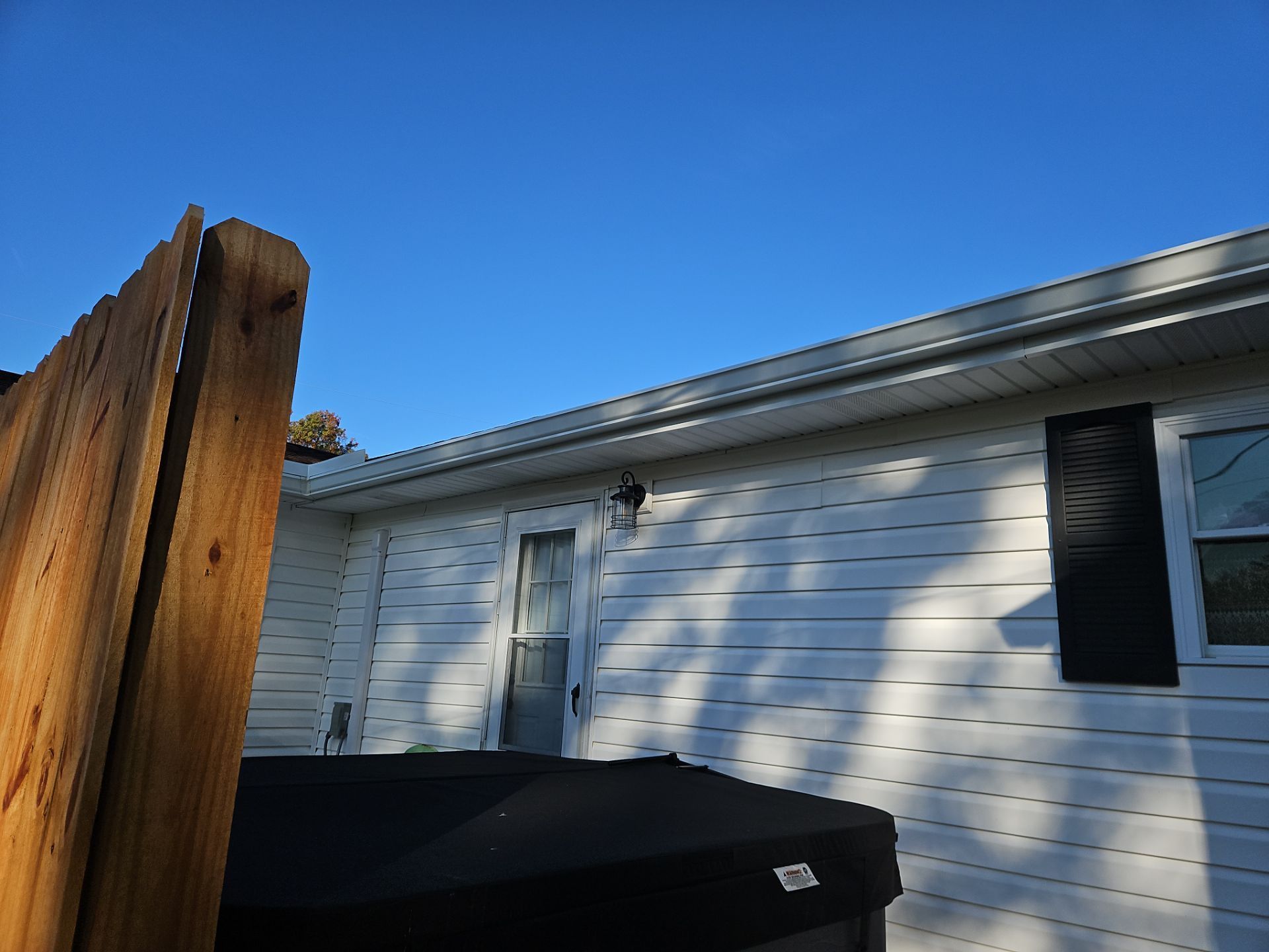 White house exterior with black dumpster and wooden fence under blue sky
