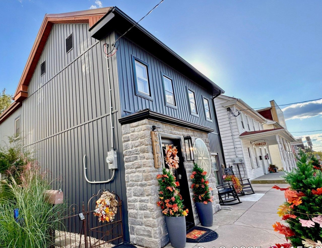 Rustic gray barn-style building with flowers by a paved walkway under a blue sky