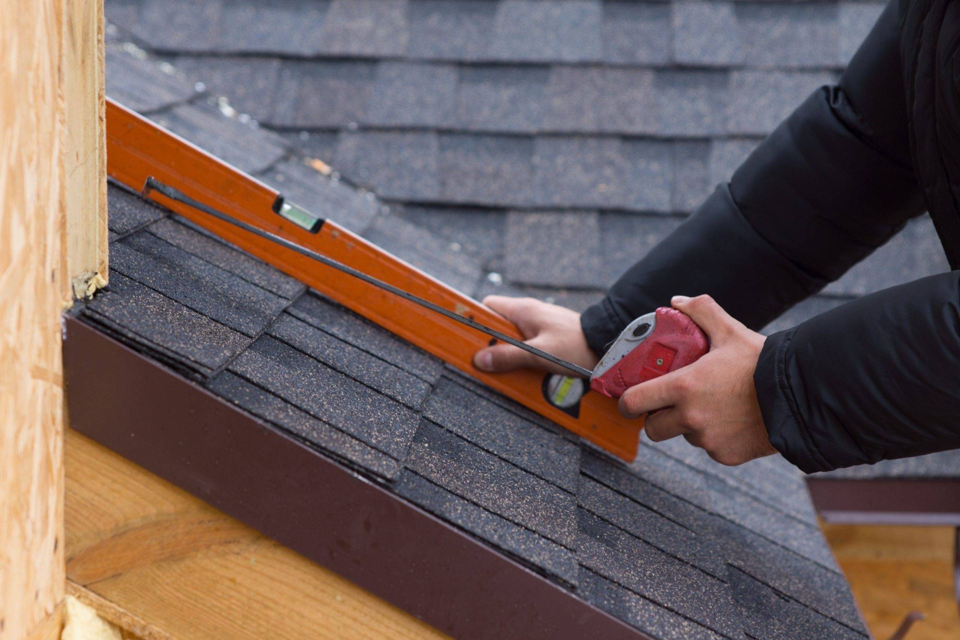 Person using a level on a shingled roof, checking for straightness.