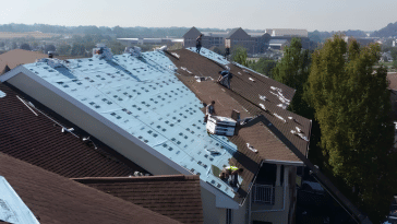 Roofers installing new shingles on a residential roof, with a partially completed section showing blue underlayment.