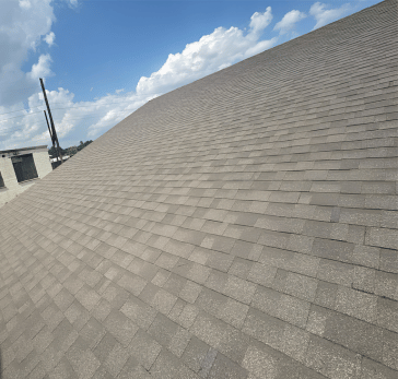 Brown shingle roof under a blue sky with fluffy white clouds, partial view of building.