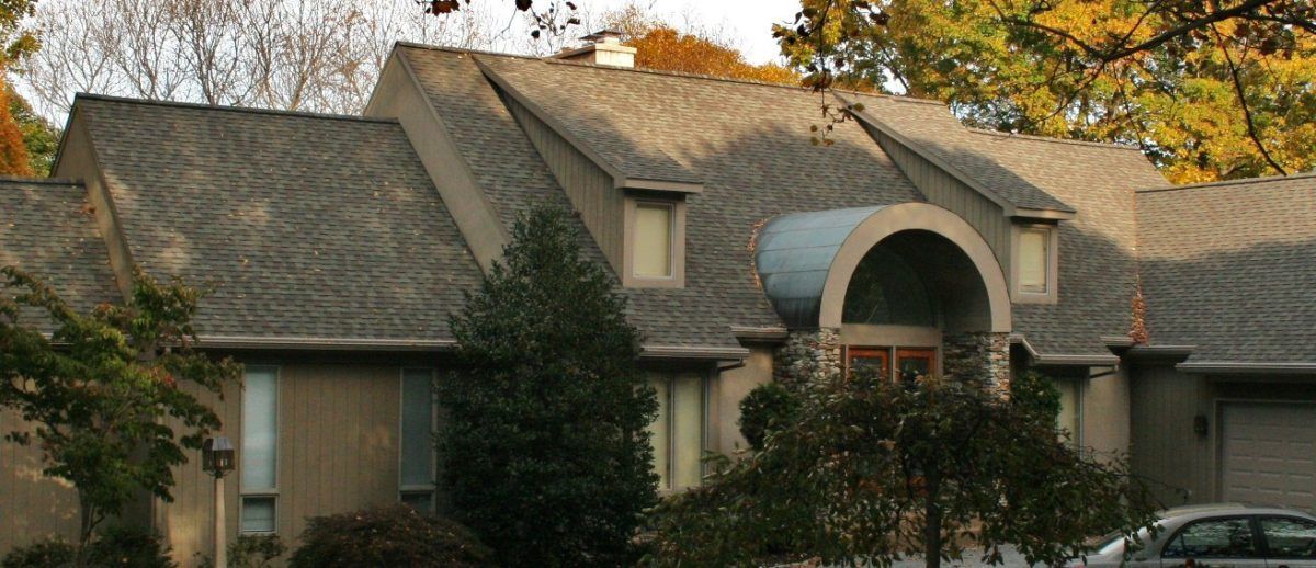 A house with a gray roof and an arched entrance, surrounded by trees.