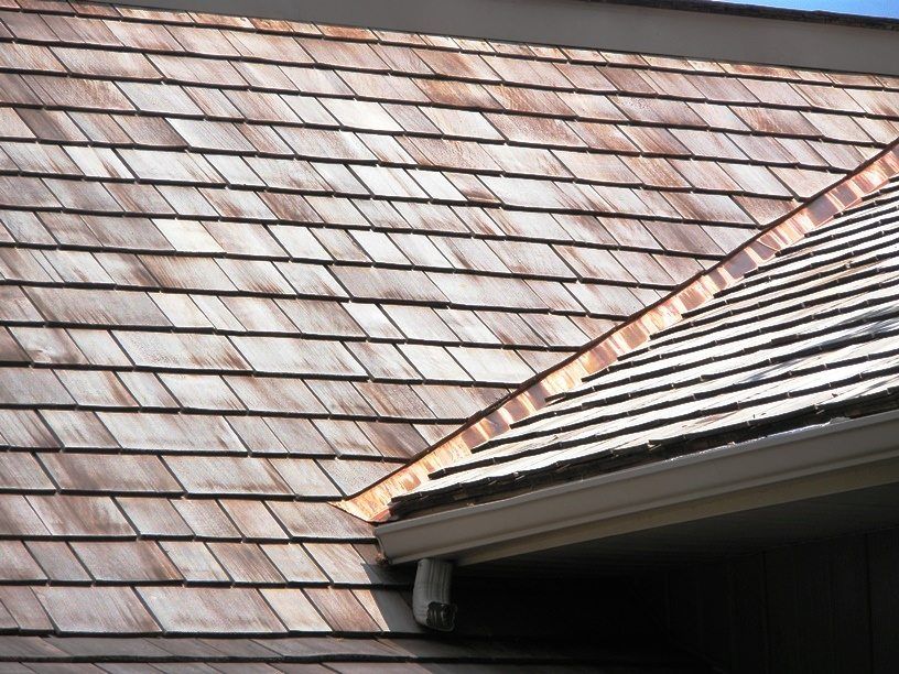 Close-up of a shingled roof with weathered brown and gray tiles and a roof edge in the foreground