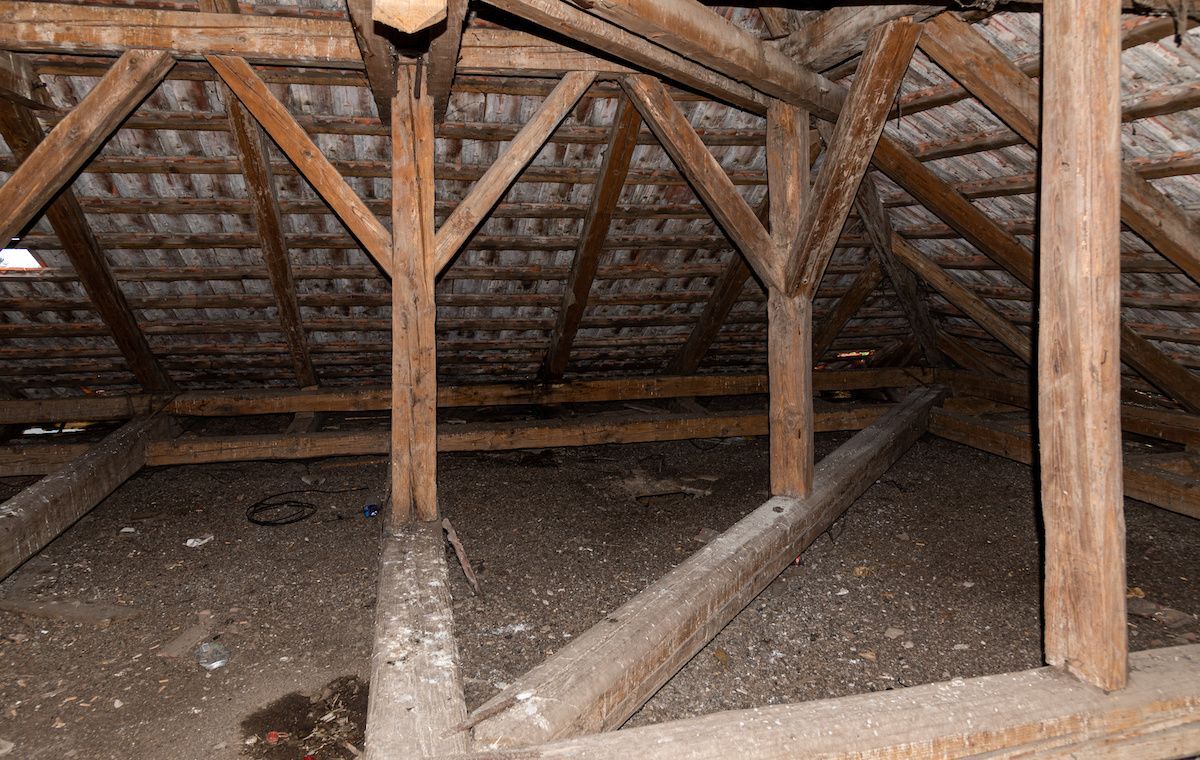 Wooden attic rafters and beams under a pitched roof with a dirt floor.