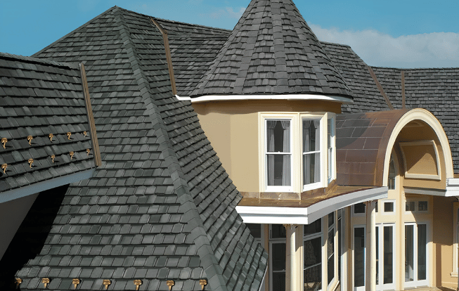 Gray shingled roof of a house with a turret and curved architectural elements. Sunny day.
