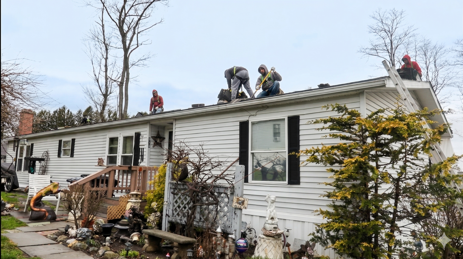 Firefighters on a white house roof, working to repair storm damage near broken trees and debris.
