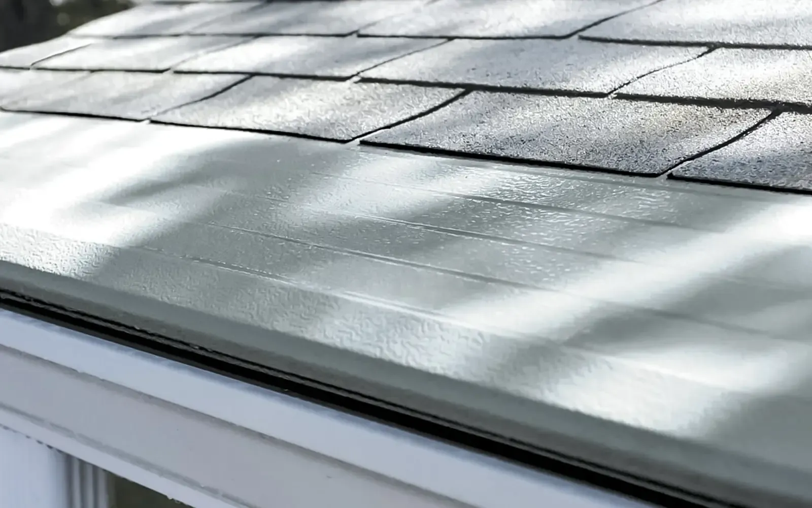 Close-up of a shingled roof with sunlight and shadows over a white soffit edge
