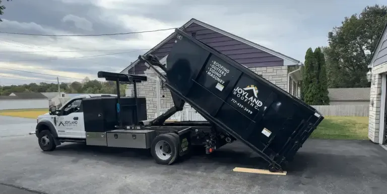A white dump truck with a raised black dumpster on a driveway.