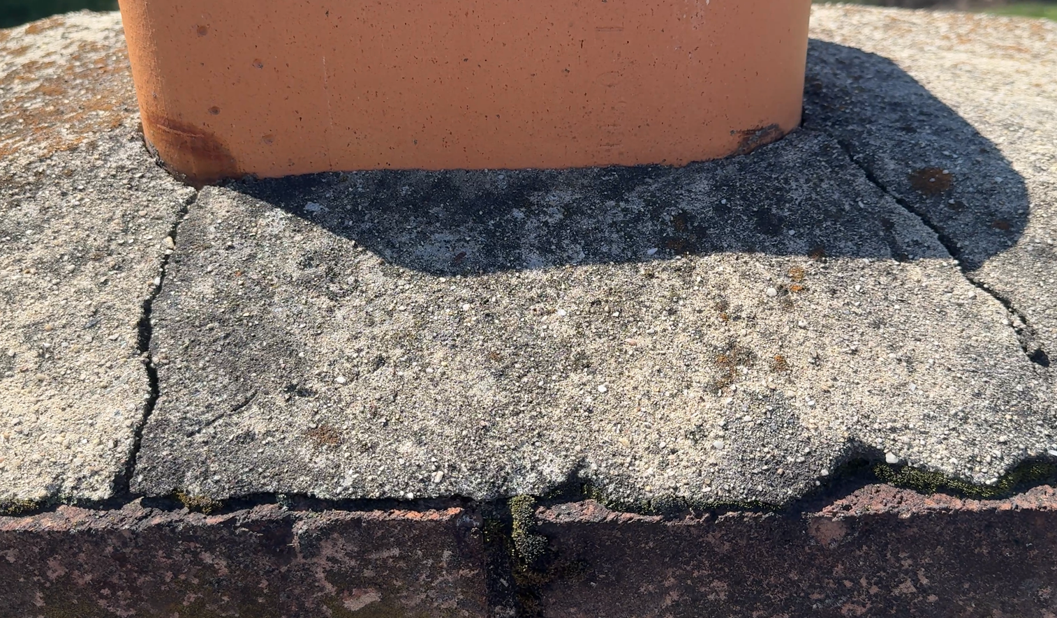 Cracked concrete base beneath a terracotta planter on a sunlit outdoor surface