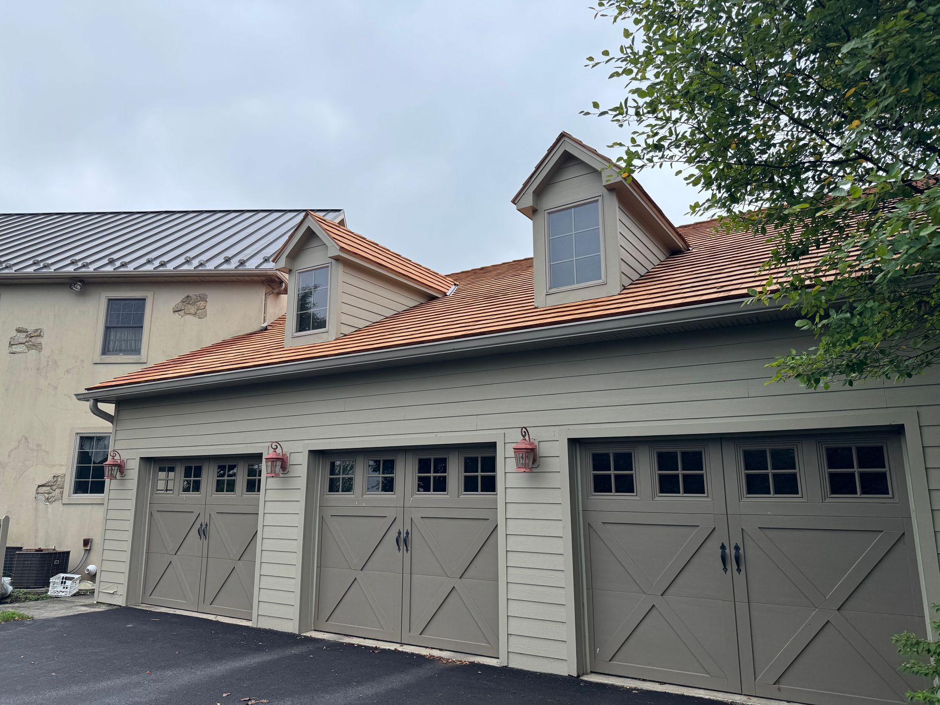 Row of gray garage doors on a beige stucco house with a terracotta tile roof and dormer windows.