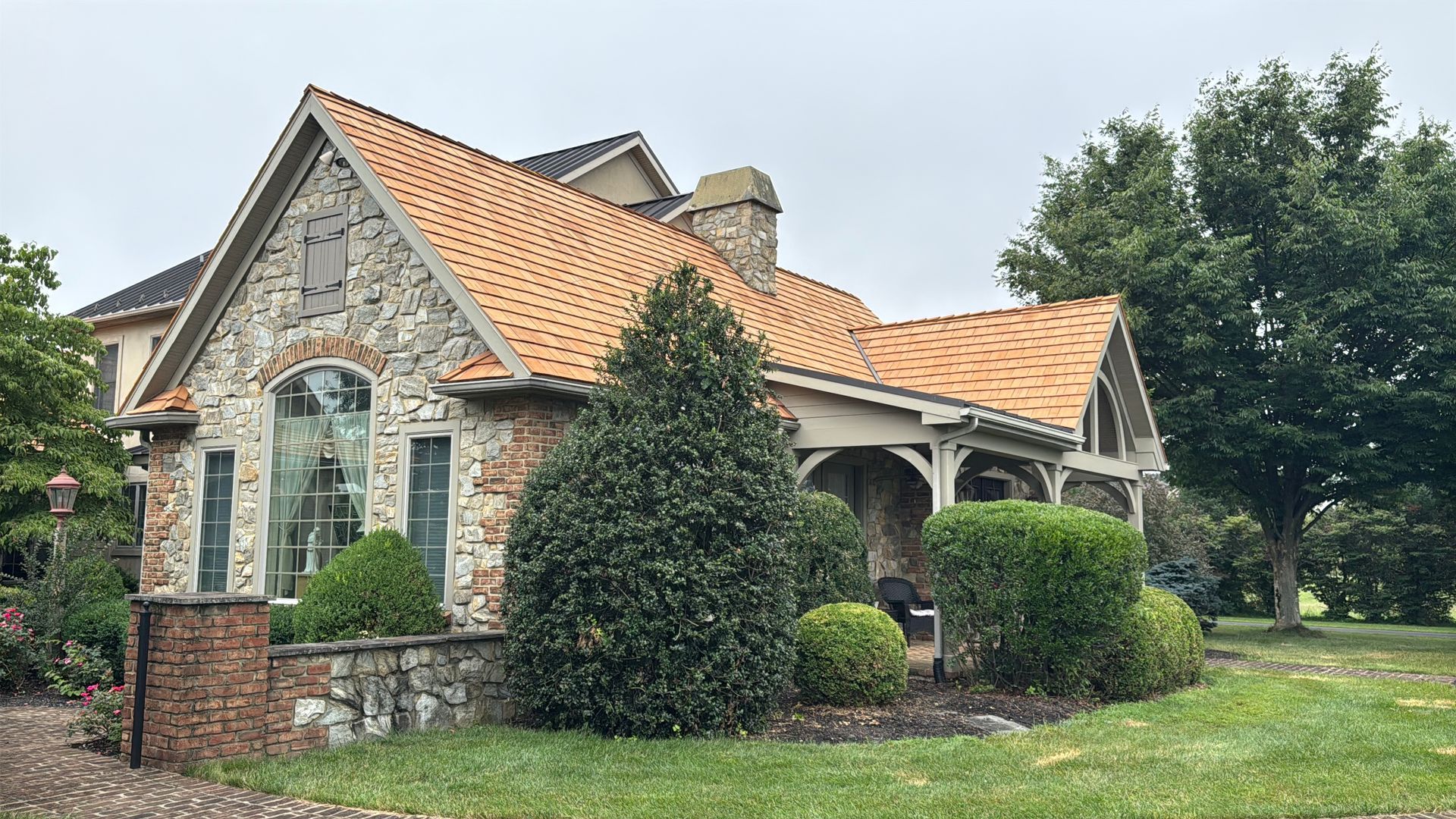 Stone house with orange-tiled roof, arched porch, and manicured shrubs on a grassy lawn