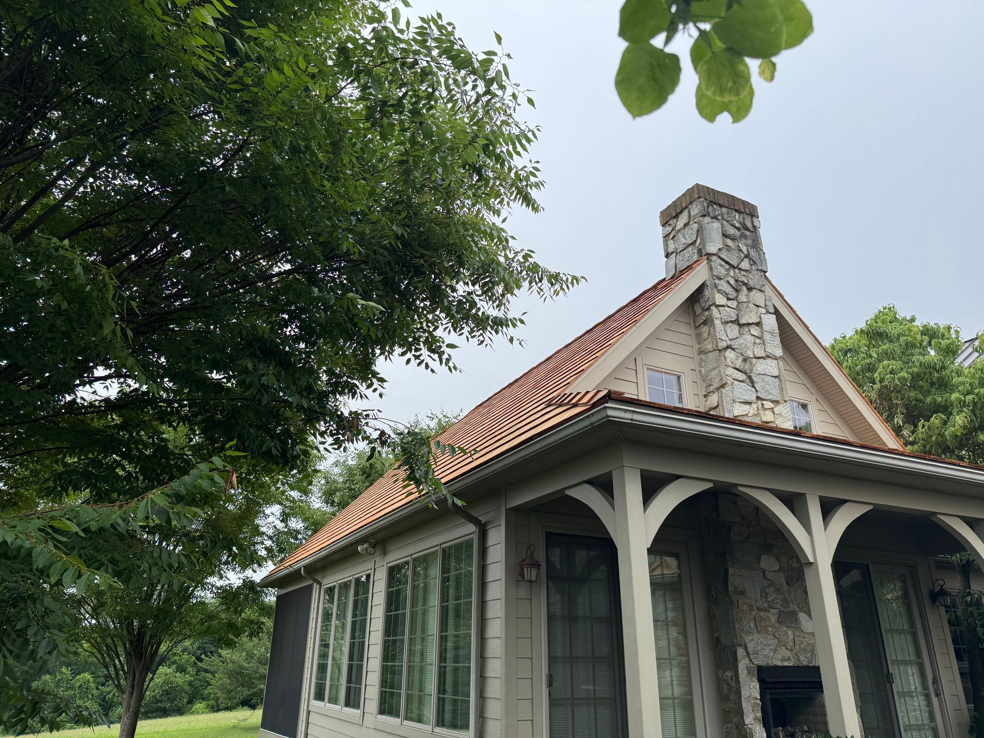 A photo showing the newly completed cedar roof of a home that Joyland Roofing Worked on. This photo shows a stone chimney, a tree and the new roof Joyland completed