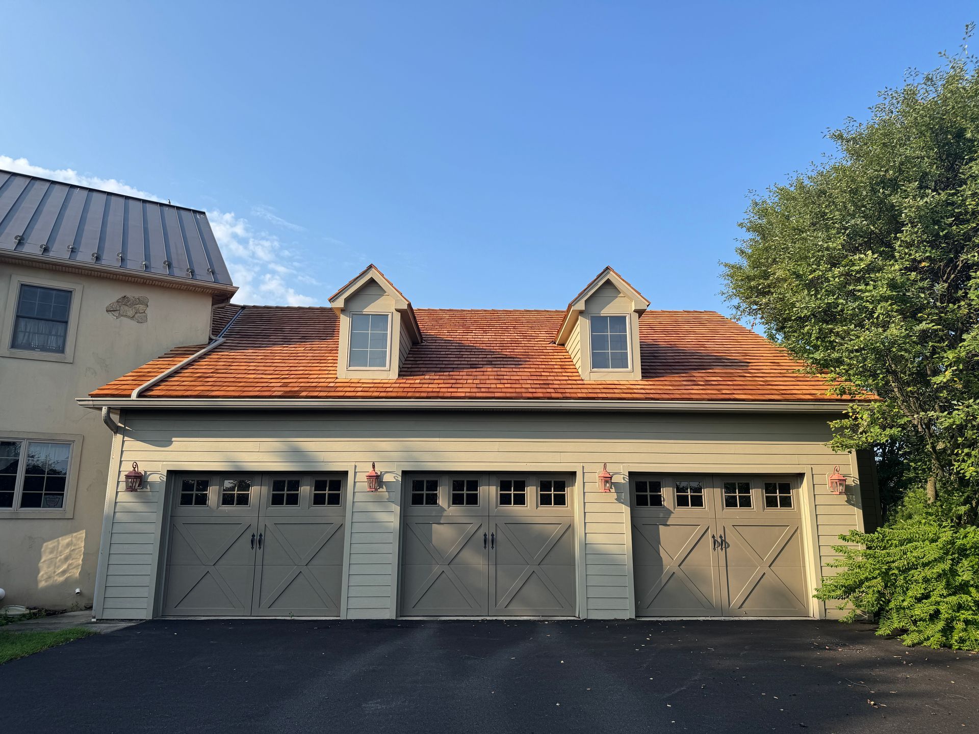 Three-car garage with gray doors, white siding, and a cedar roof under a blue sky