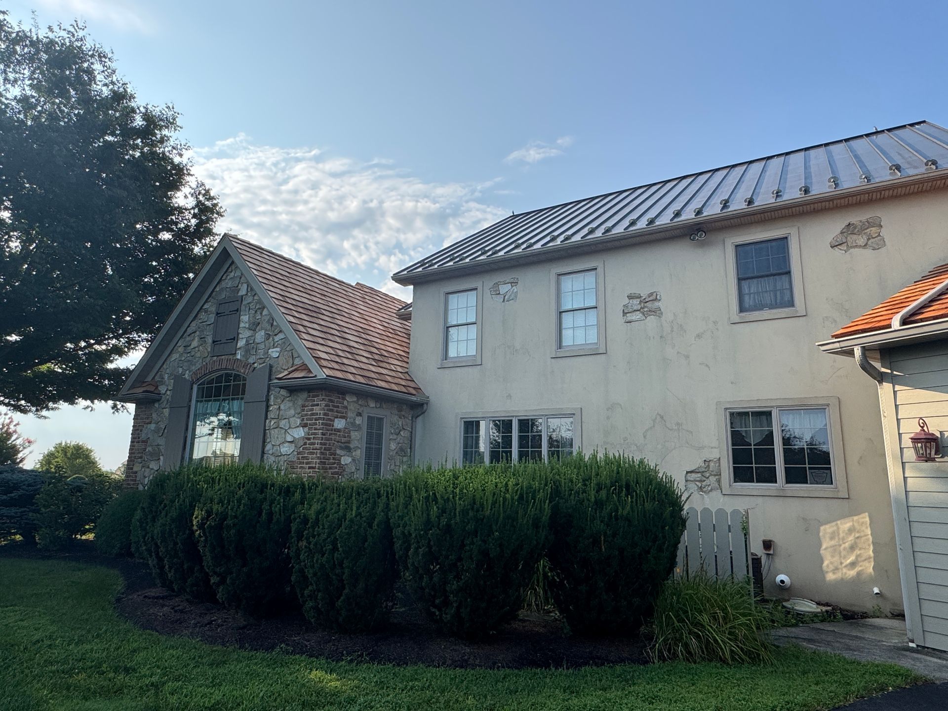 Stone house with cedar roofs and trimmed hedges in a sunny yard