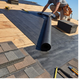 Roofer installing protective underlayment over a wood roof deck during an asphalt shingle replacement
