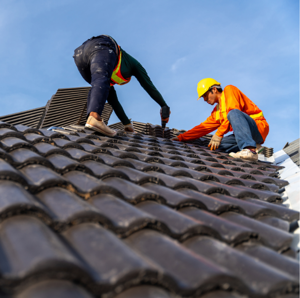 Two roofers installing dark ceramic tiles on a rooftop on a sunny day.