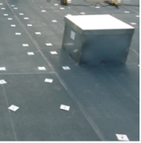 A large, silver box sits on a dark surface marked with evenly spaced white squares.