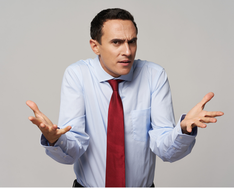 Man in a blue shirt and red tie gestures with both hands up, looking confused.