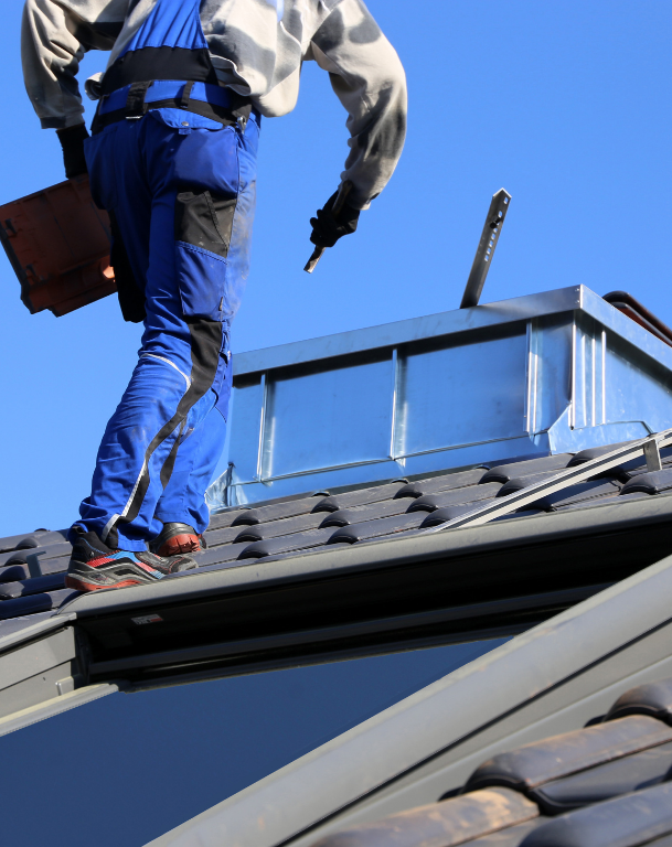 Worker on a rooftop near a chimney, wearing blue pants and safety harness.