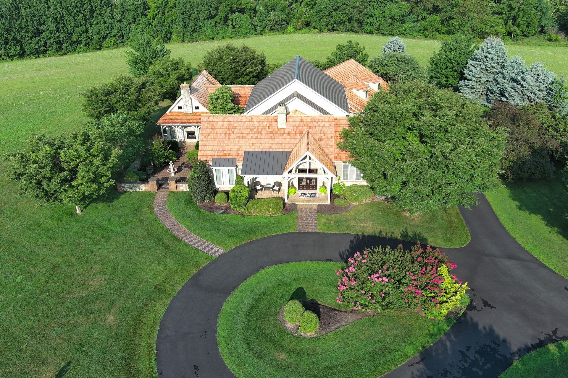 Aerial view of a large house with cedar roofs, surrounded by trees, lawns, and a curved driveway.