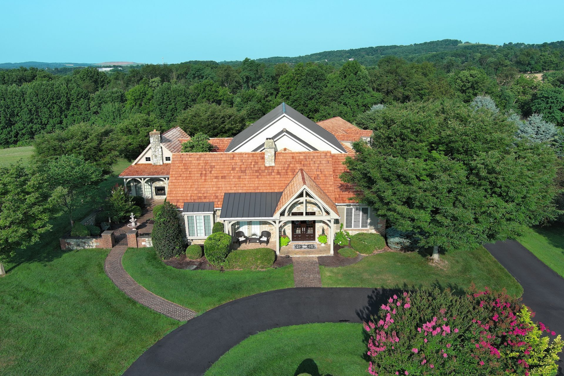 Aerial view of a large house with cedar roofs, surrounded by trees and a winding driveway