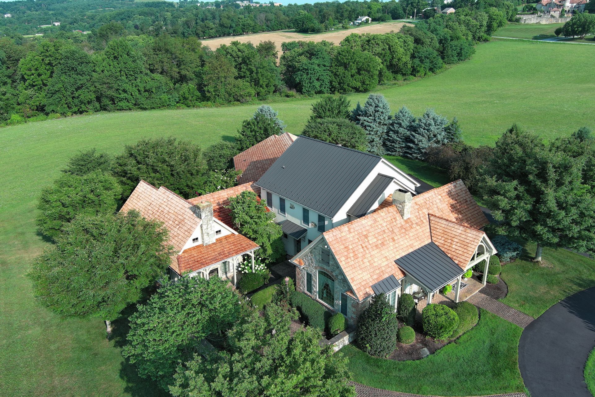 Aerial view of a rural house with red-tile roofs, surrounded by green fields and trees