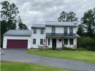 White two-story house with red garage door and roof. Porch with red posts, star decor, on a cloudy day.