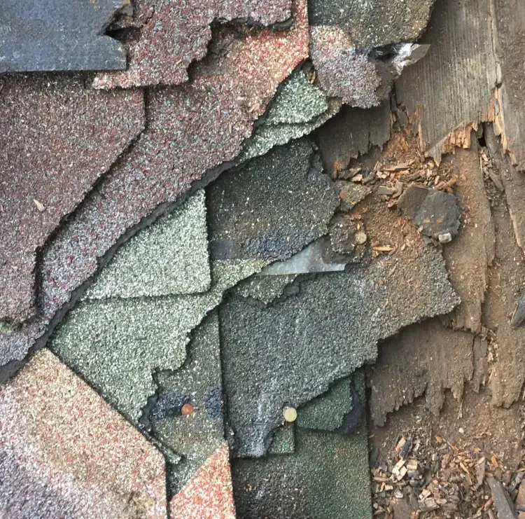 Close-up of layered, peeling roof shingles in gray, green, and brown tones