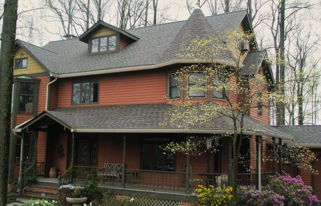 Two-story reddish-brown house with a porch, surrounded by trees.