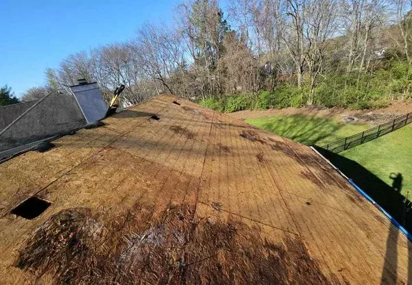 View of a damaged roof with exposed underlayment and debris; sunny day.
